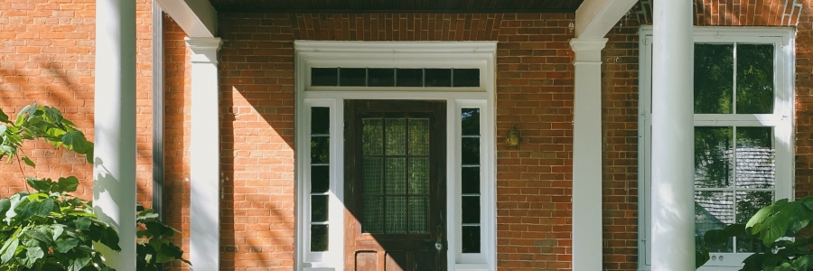 an older orange brick home with a white porch, gray steps and a dark brown wooden door