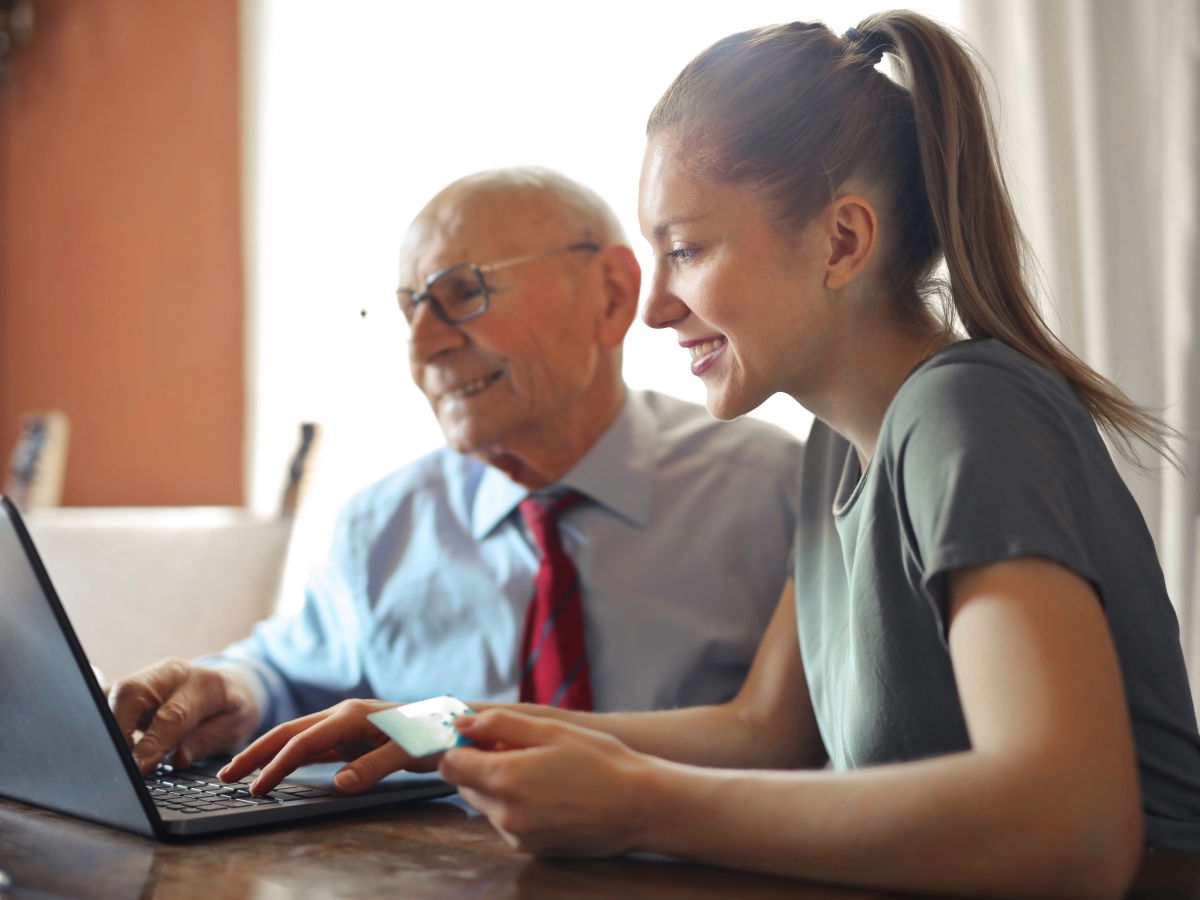 a young woman is assisting an elderly gentleman to make a payment on a laptop