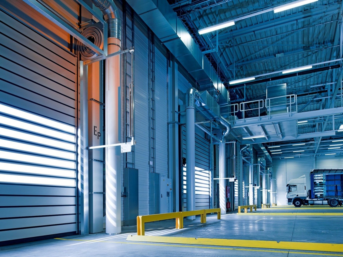 A warehouse with a concrete floor, yellow marked out parking spots and large roll-up bay doors.