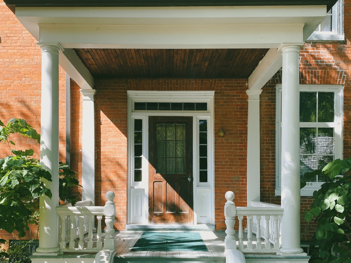 Energy Retailers an older orange brick home with a white porch, gray steps and a dark brown wooden door