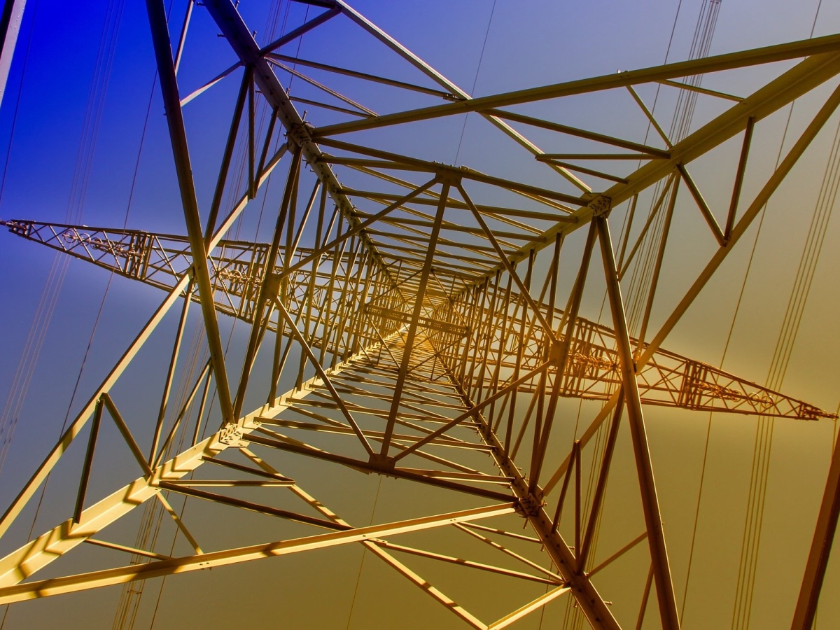 A picture of a steel transmission line tower as it would look from underneath when staring at the sky. The background fades from blue to yellow, top left to bottpm right.
