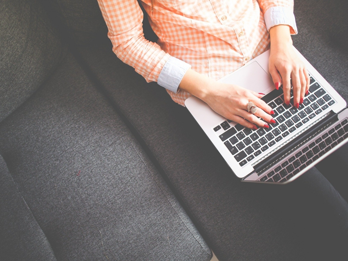 SST2 A person wearing an orange and white gingham patterned shirt works on a laptop while seated on a gray couch