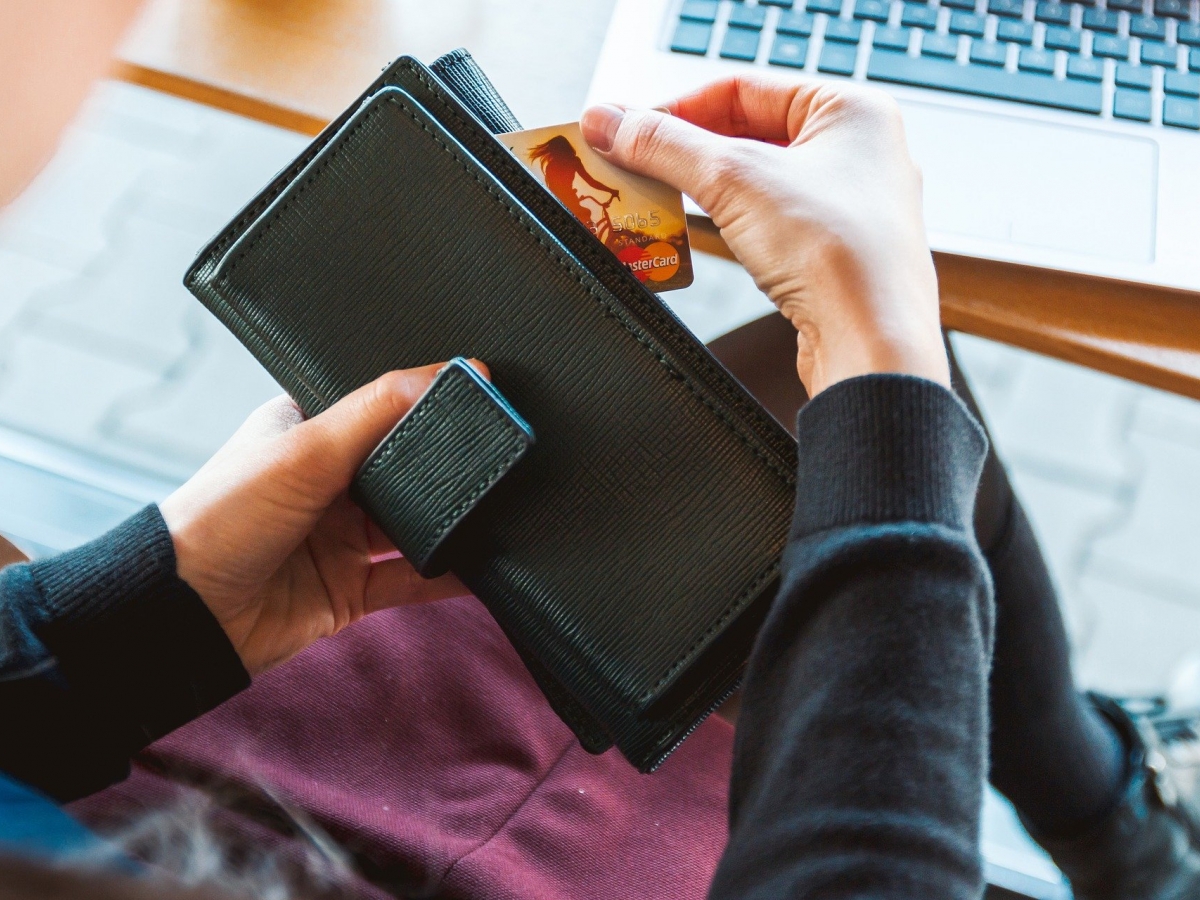 Payment Methods Picture of a person's hands holding a black wallet with a mastercard partially removed
